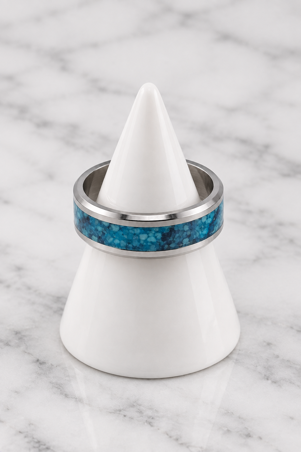 Silver ring with blue inlay on white porcelain cone, marble background