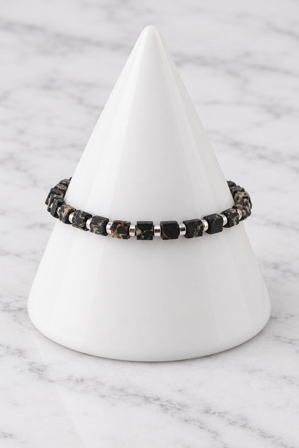 Black marbled cube bead bracelet on white porcelain cone, marble background