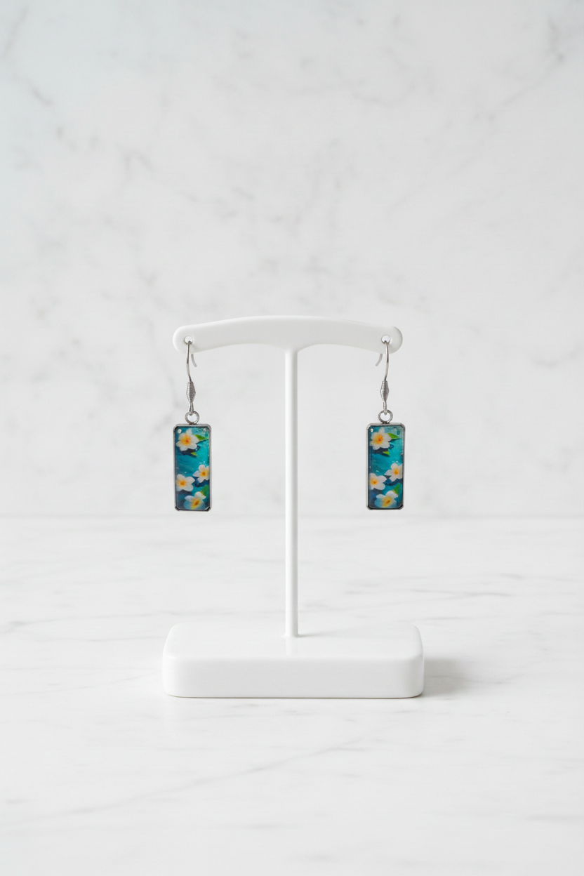 Corrected frangipani earring pair on white porcelain stand