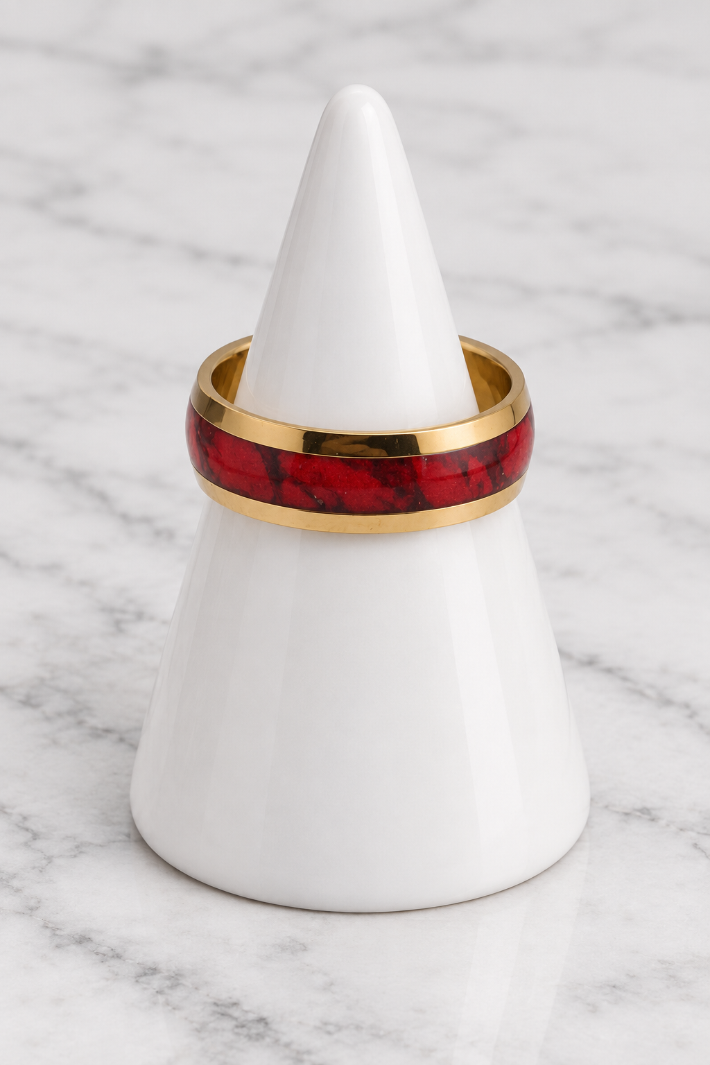 Gold red inlay ring on white porcelain cone, marble background