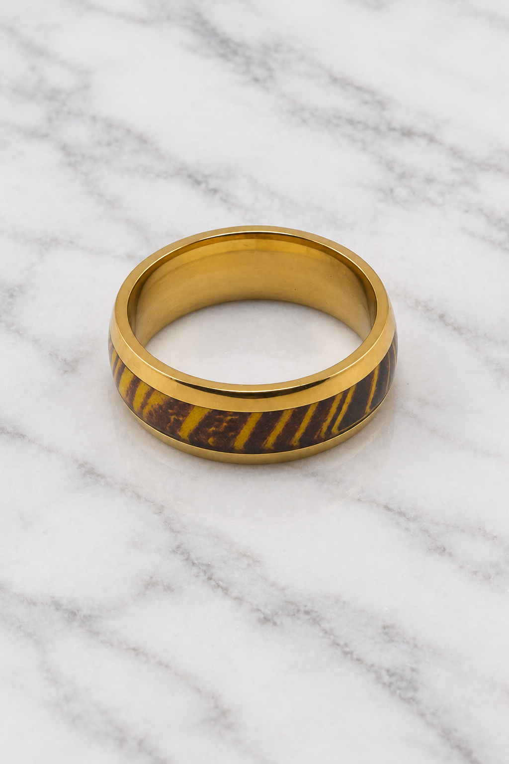 Gold ring with brown and gold striped inlay flat lay on white marble