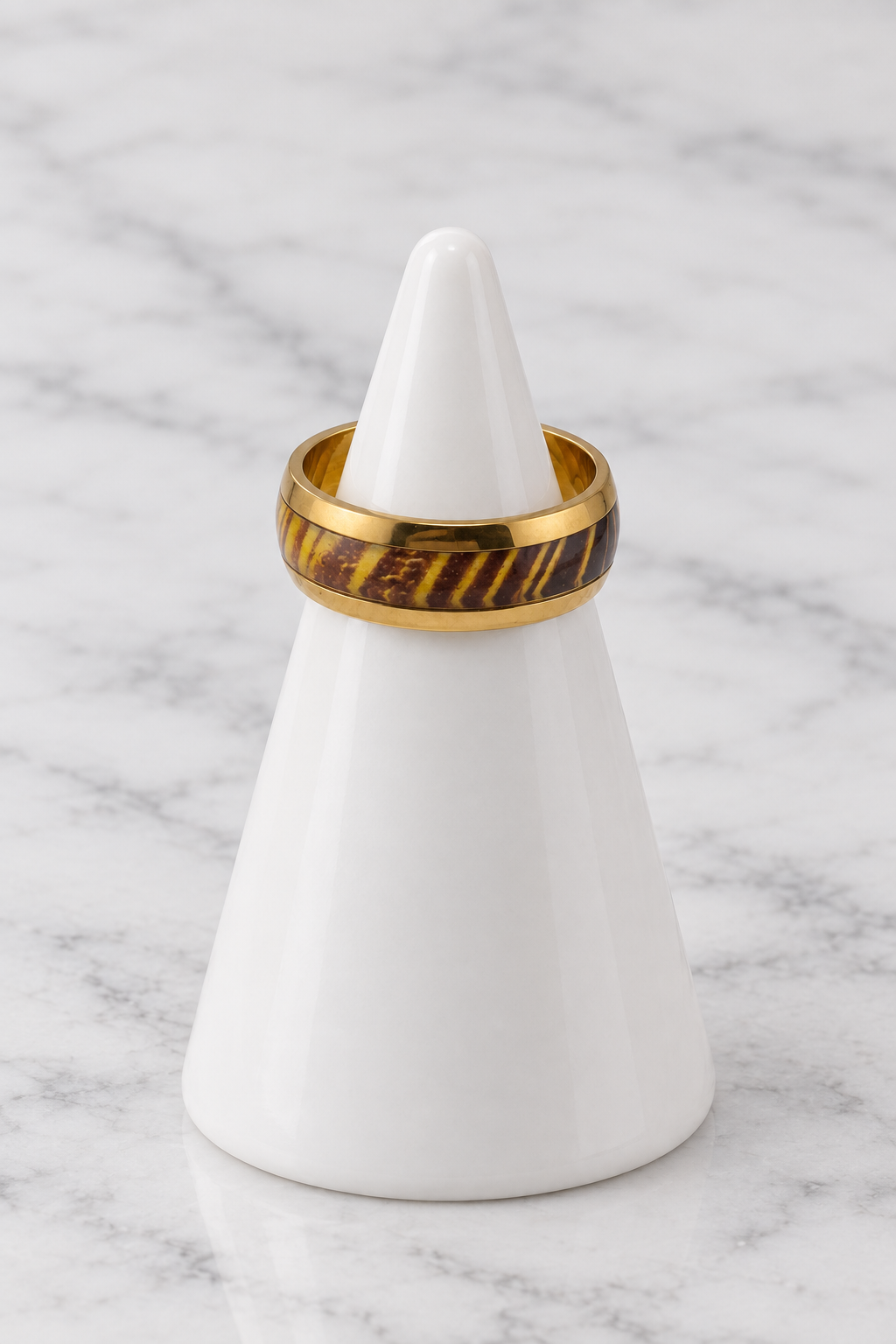 Gold ring with brown and gold striped inlay on white porcelain cone, marble background