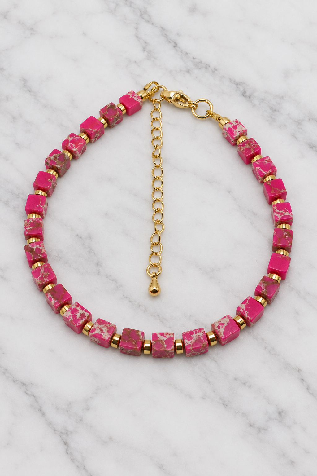 Pink cube bead bracelet with gold spacers flat lay on white marble