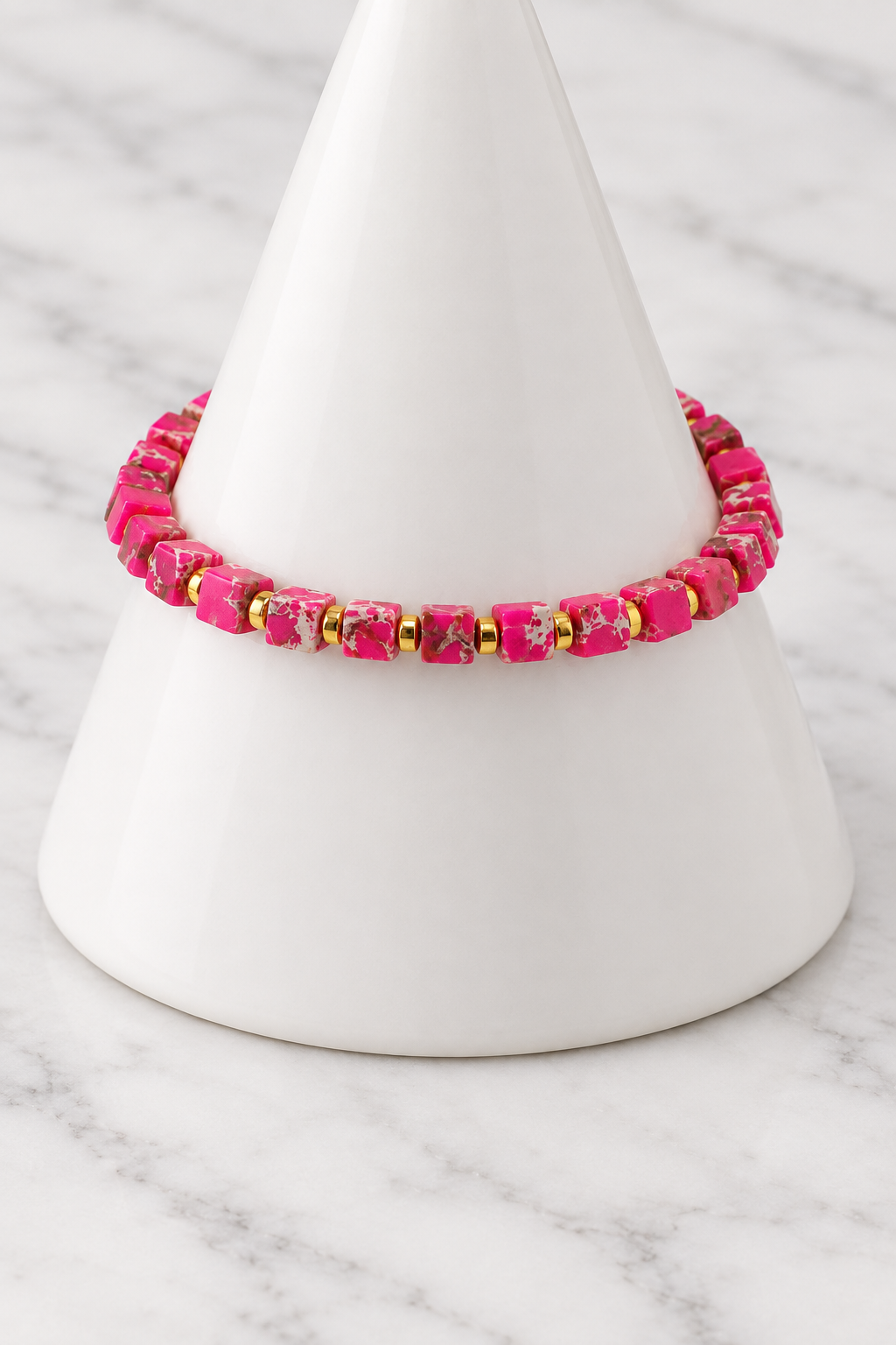 Pink cube bead bracelet with gold spacers on white porcelain cone